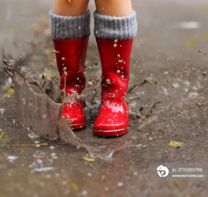 穿着红色雨靴的孩子跳进水坑