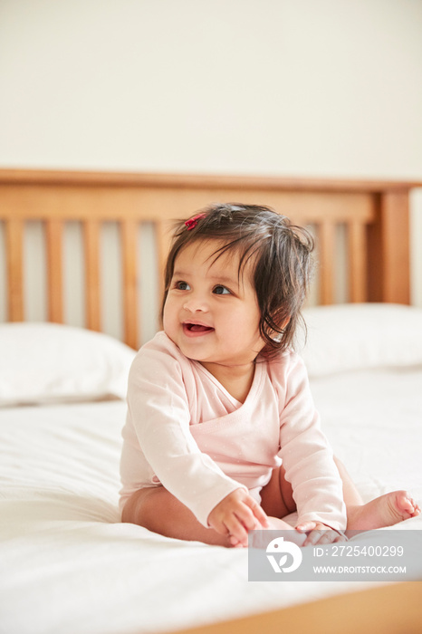 Happy baby girl sitting up on bed playing with her feet