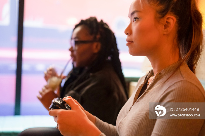 Female friends drinking cocktails and playing in video games at pub