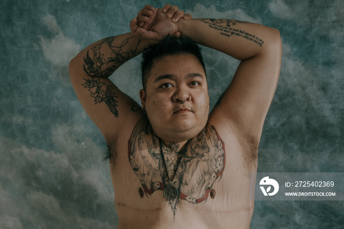 portrait of a plus size asian non-binary person with arms overhead