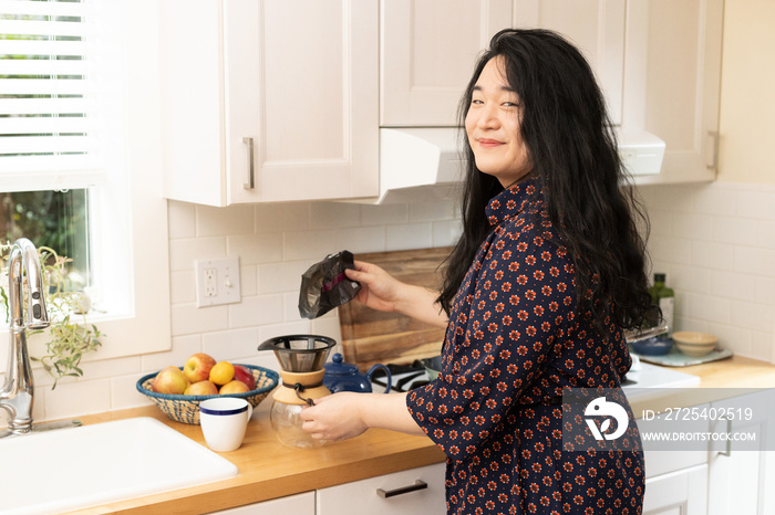 Asian trans woman prepares coffee in the kitchen.