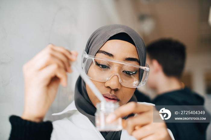 Serious female student wearing hijab doing scientific experiment in chemistry class at university