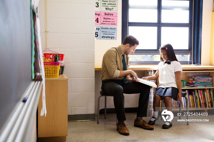 Teacher helping schoolgirl (6-7) with homework in classroom