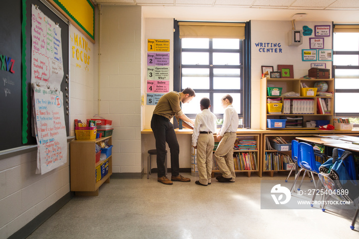 Male teacher and two schoolboys (8-9) standing by windowsill in classroom