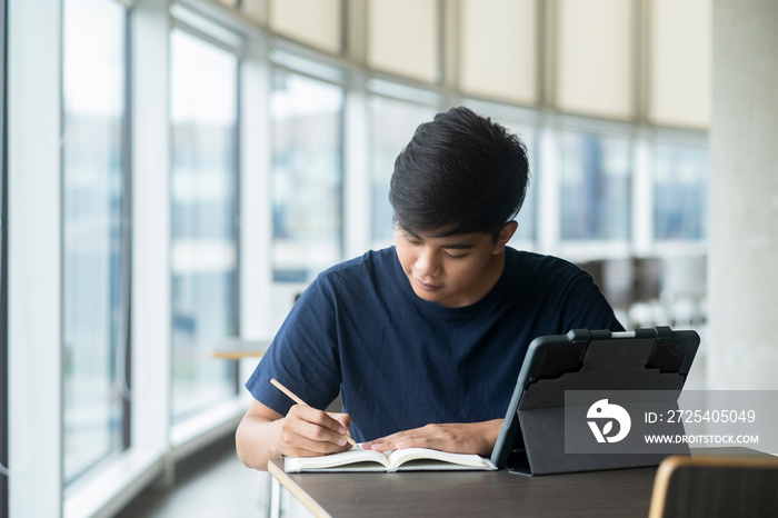 Young collage student using computer and mobile device studying online.