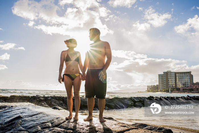 Young couple holding hands on rocks at Waikiki Beach, Hawaii, USA