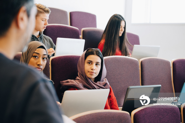 Multi-ethnic students with laptop listening to professor during lecture in class