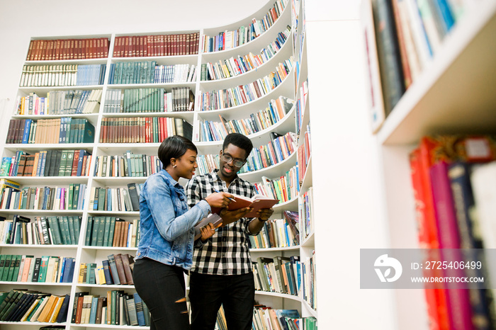 young Afro-American students reading book between the shelves in the library