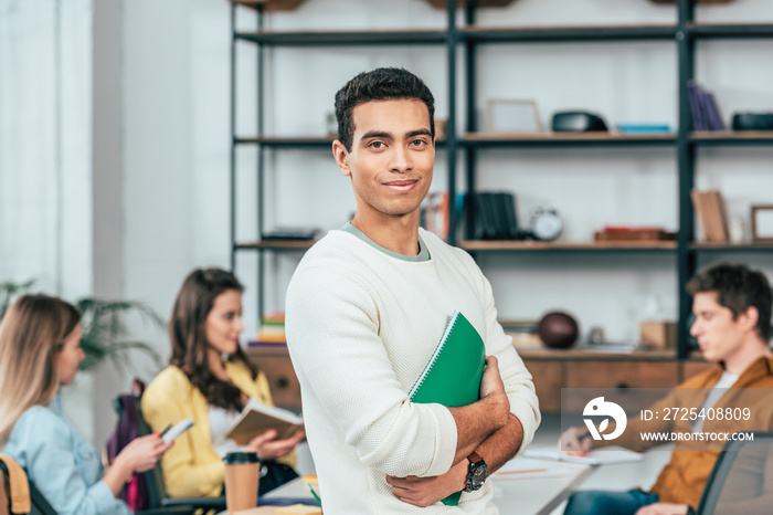 Smiling student holding green notebook and looking at camera