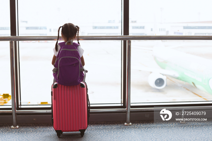 Cute asian child girl with backpack looking at plane and waiting for boarding in the airport