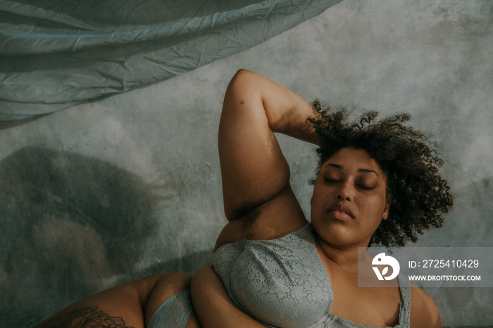 portrait of a plus size afro indigenous person lying on hip with hand in hair