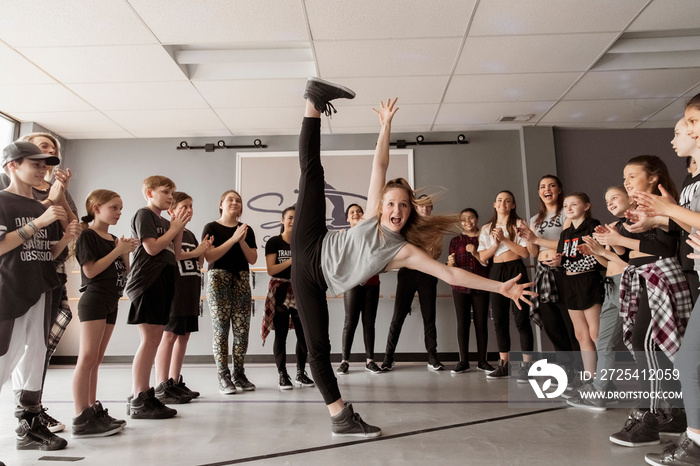 Dancers cheering young woman screaming while standing on one leg in dance studio