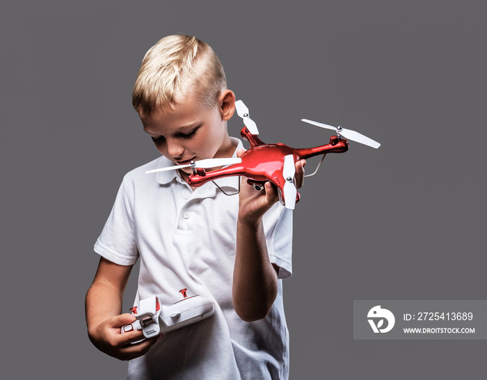 Handsome little boy boxer with blonde hair dressed in a white t-shirt holds a quadcopter and control