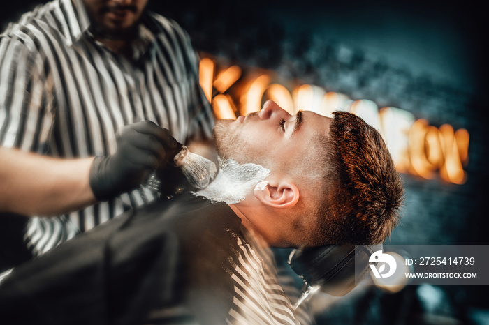 Modern and vintage barbershop with dark stylish brickwalls and barber which preparing his client for