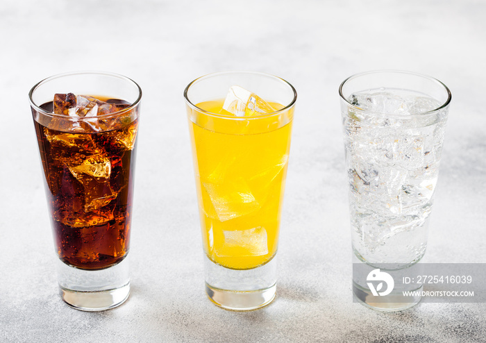 Glasses of soda drink with ice cubes and bubbles on stone kitchen table background. Cola and orange 