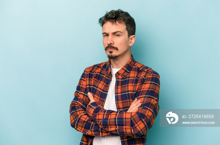 Young caucasian man isolated on blue background suspicious, uncertain, examining you.