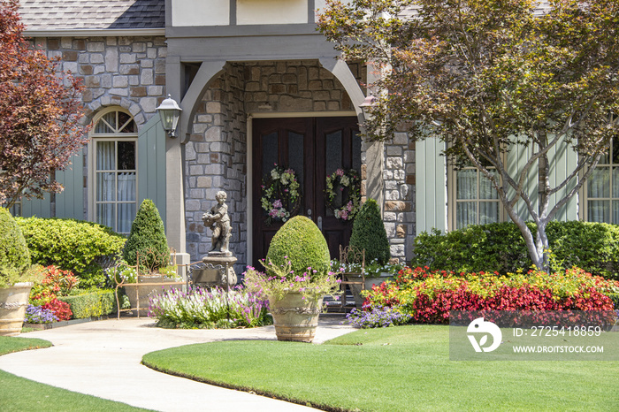 Entrance to upscale rock house with beautiful landscaping and a statue and wreaths and benches besid