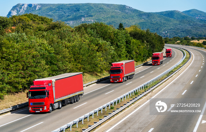 Caravan or convoy of Four red Lorry Lorry trucks in line on a country highway under a beautiful sky