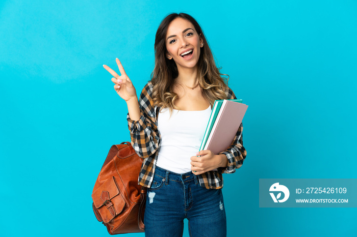 Young student woman isolated on blue background smiling and showing victory sign