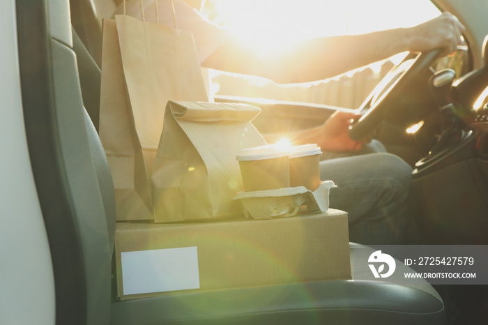 Blank box, coffee cups, paper packages and courier in car. Delivery