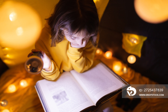 Young female child reading encyclopedia in a home made livingroom tent with light balls.
