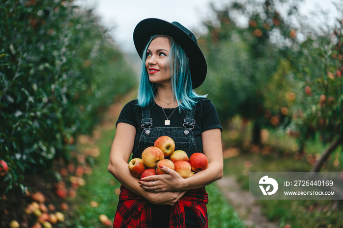 Blue haired woman picked up a lot of ripe red apple fruits from tree in green garden. Organic lifest