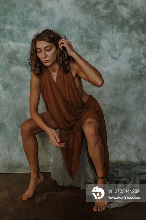 portrait of a non-binary person sitting on a box leaning forward tucking hair behind ear