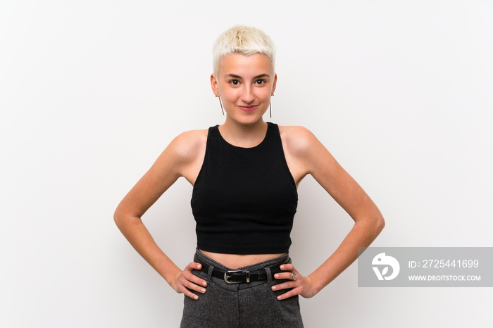 Teenager girl with short hair over white wall posing with arms at hip and smiling