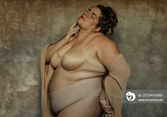 portrait of a plus size woman with curly hair standing with hand on chin