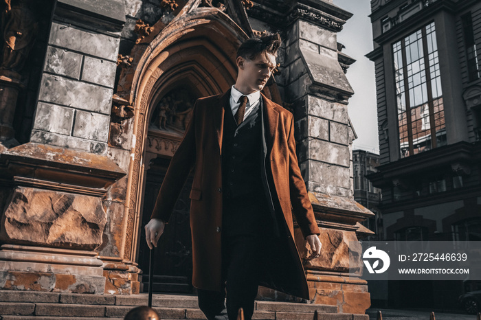 Handsome young model portrait on city street. Stylish man in full suit and coat with cane walking on