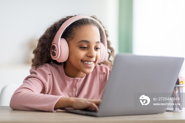Z世代非洲裔美国女学生使用笔记本电脑，戴着耳机，面带微笑