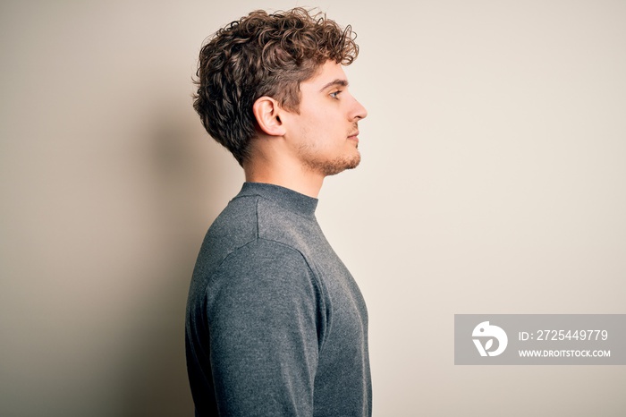 Young blond handsome man with curly hair wearing casual sweater over white background looking to sid