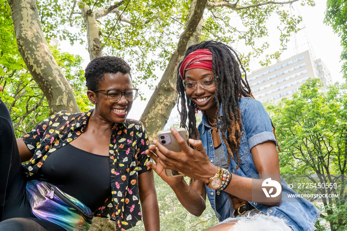 Two smiling young women looking at smart phone in park