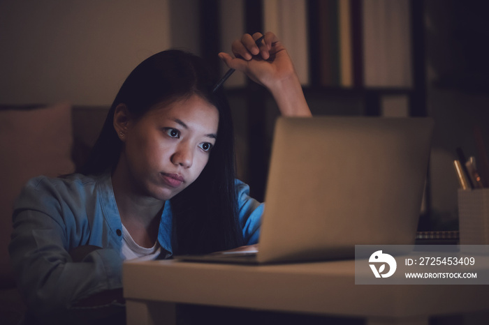 亚洲女学生或女商人晚上工作到很晚。注意力集中，坐在办公桌前昏昏欲睡