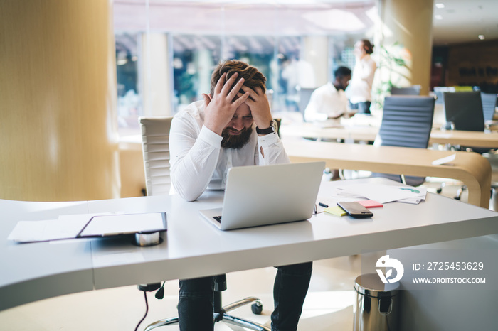 Overworked male employee holding head feeling pain during working process stressed about problems, w