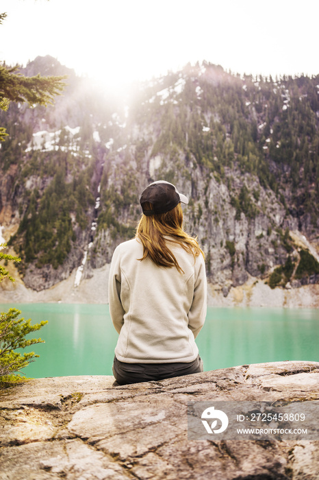 坐在山上靠湖的女人的后视图