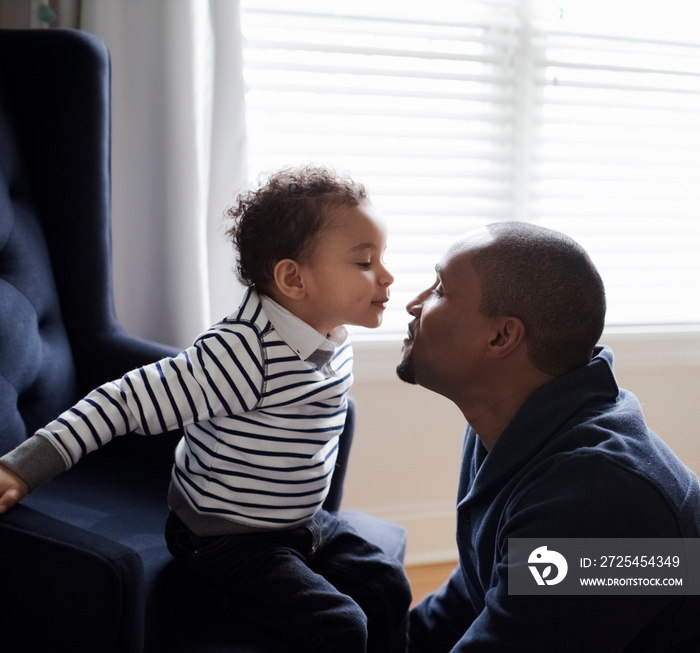 Side view of son kissing father while sitting on armchair at home