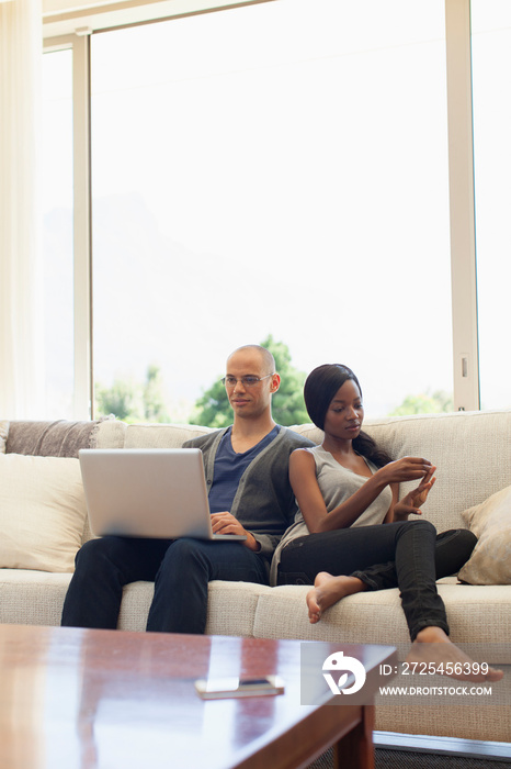 Young couple using laptop and smart phone on sofa