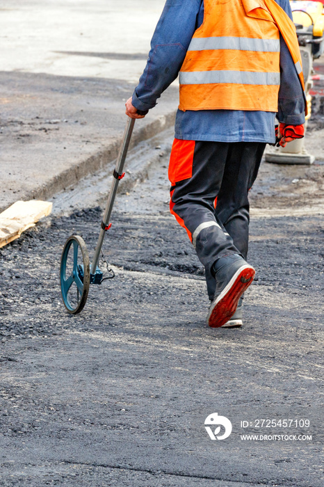 A road service worker measures the jobsite with an electronic measuring wheel.