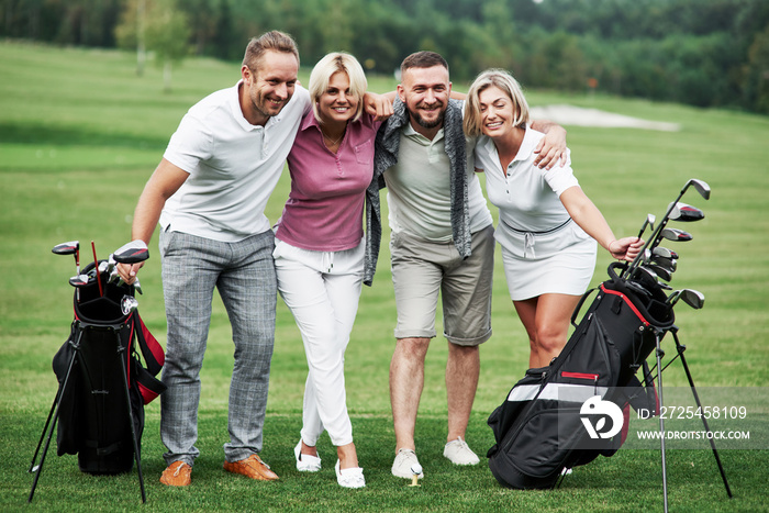 Beautiful woods at background. Photo of friends hugging and smiling with golf equipment after the ga