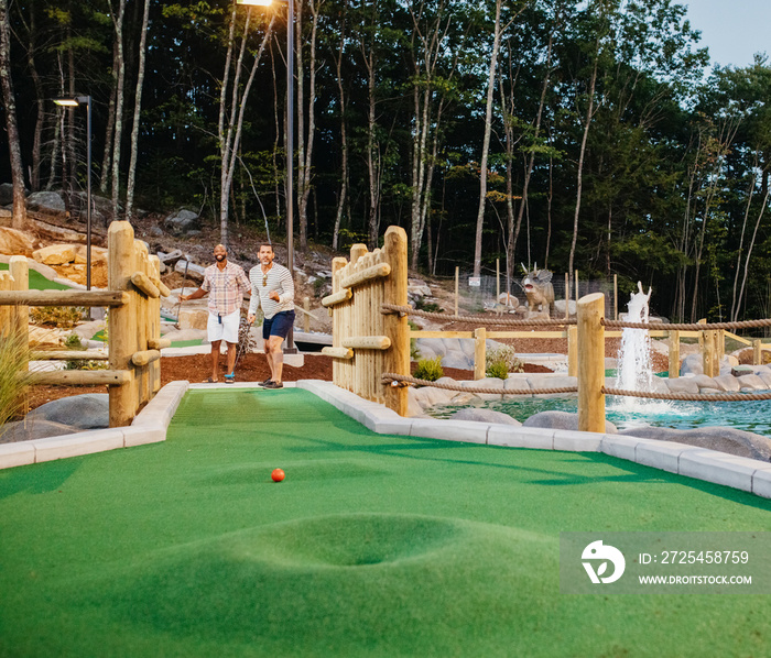 Friends looking at golf ball on grass at miniature golf course