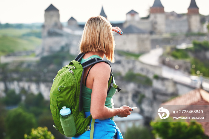 背着绿色背包的女游客拍摄一座古老城堡的照片。度假和夏季旅行