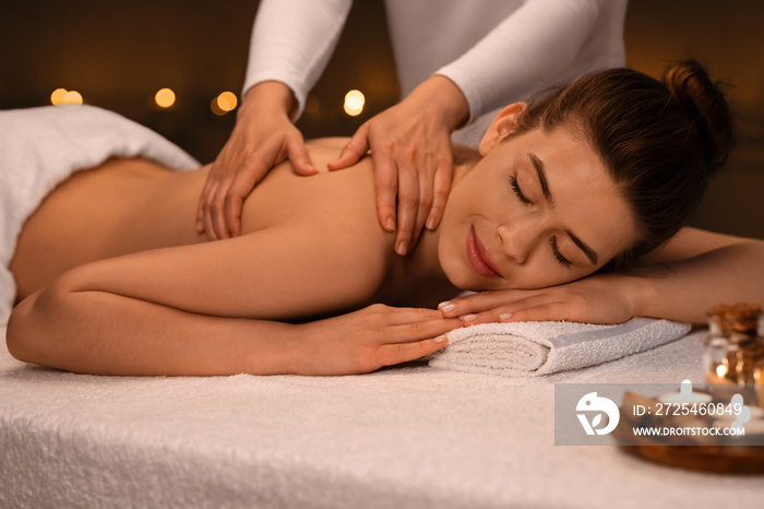 Massage therapist hands rubbing girl shoulders, spa interior