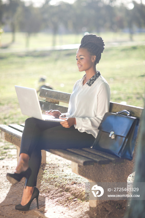 Business woman using laptop on park bench