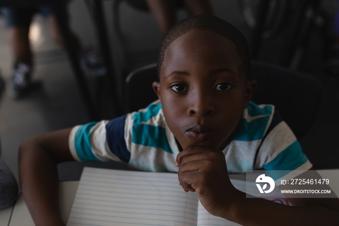 Close-up of black schoolboy with hand on chin sitting at desk