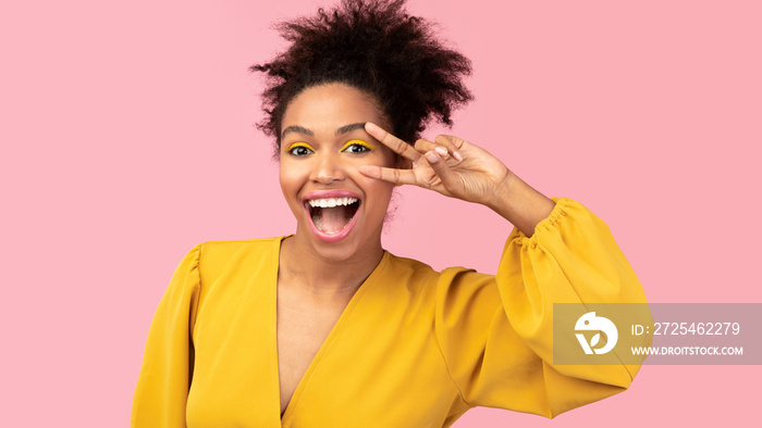 Happy black woman showing v sign at studio