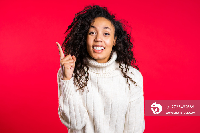 Portrait of young thinking pondering afro woman having idea moment pointing finger up on red studio 