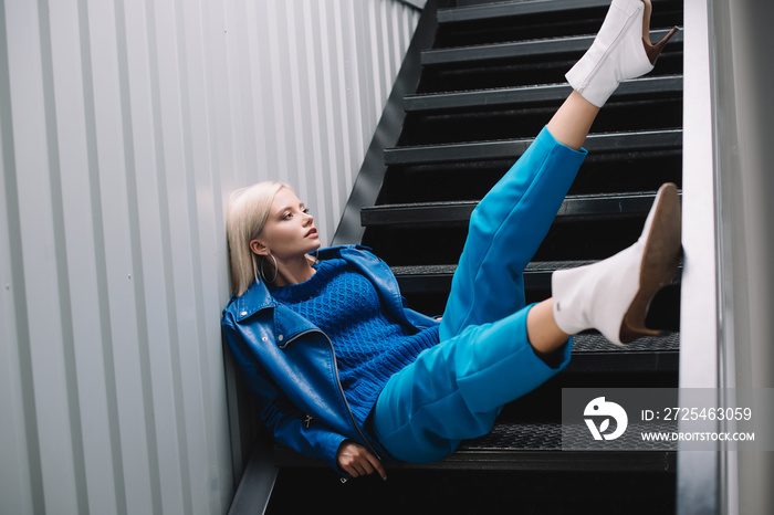 blonde woman wearing blue leather jacket and heels sitting on stairs