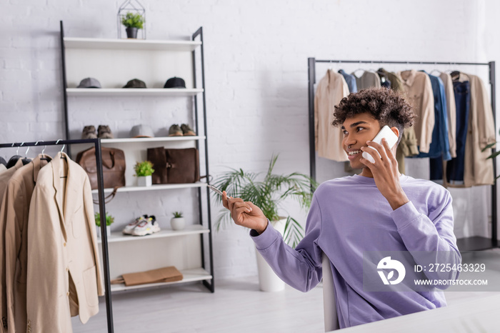 Cheerful african american owner of showroom holding pen and talking on smartphone