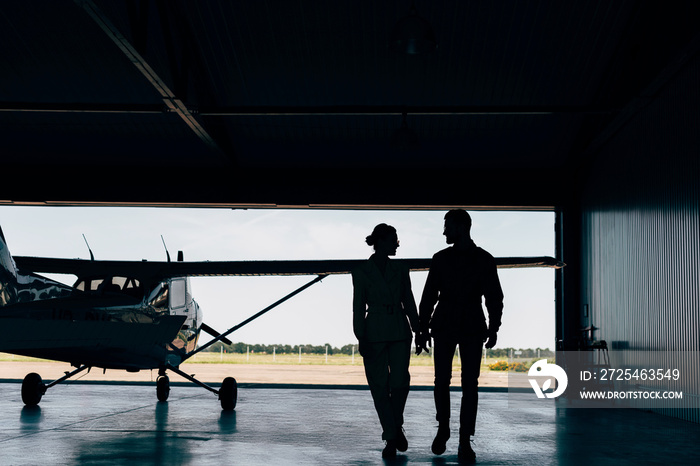 年轻夫妇在机库里走在飞机附近的侧影后视图